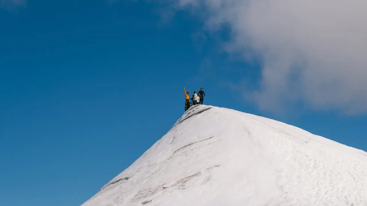 Vandrare på toppen av en snötäckt bergstopp, en vy som ger en känsla av var ligger Kebnekaise.