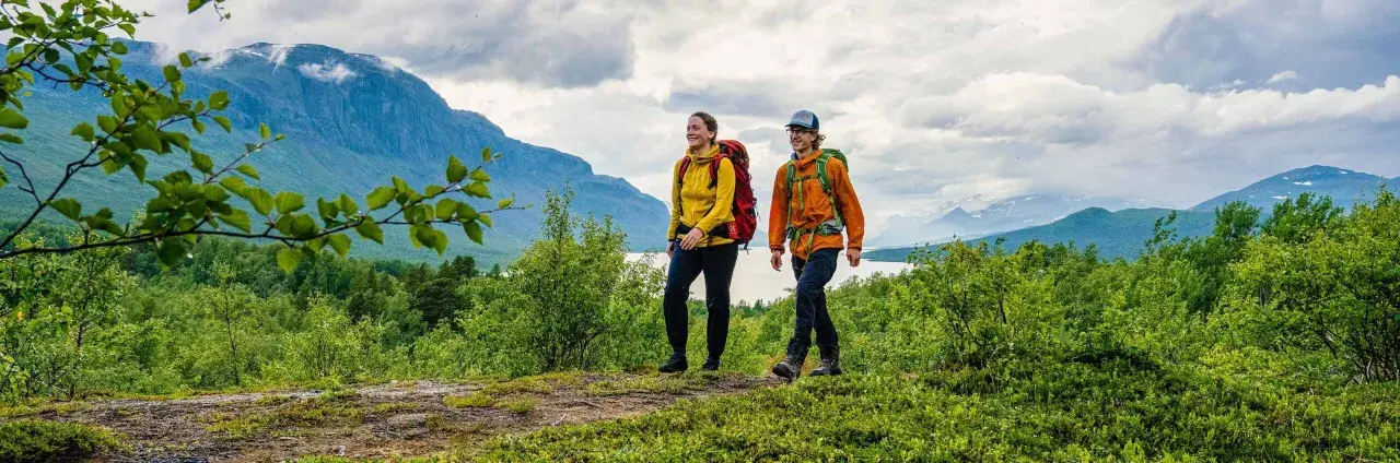 Två glada vandrare med ryggsäckar på en stig i fjällen. En perfekt plats att bo på efter en dag av vandring, kanske på ett STF vandrarhem.
