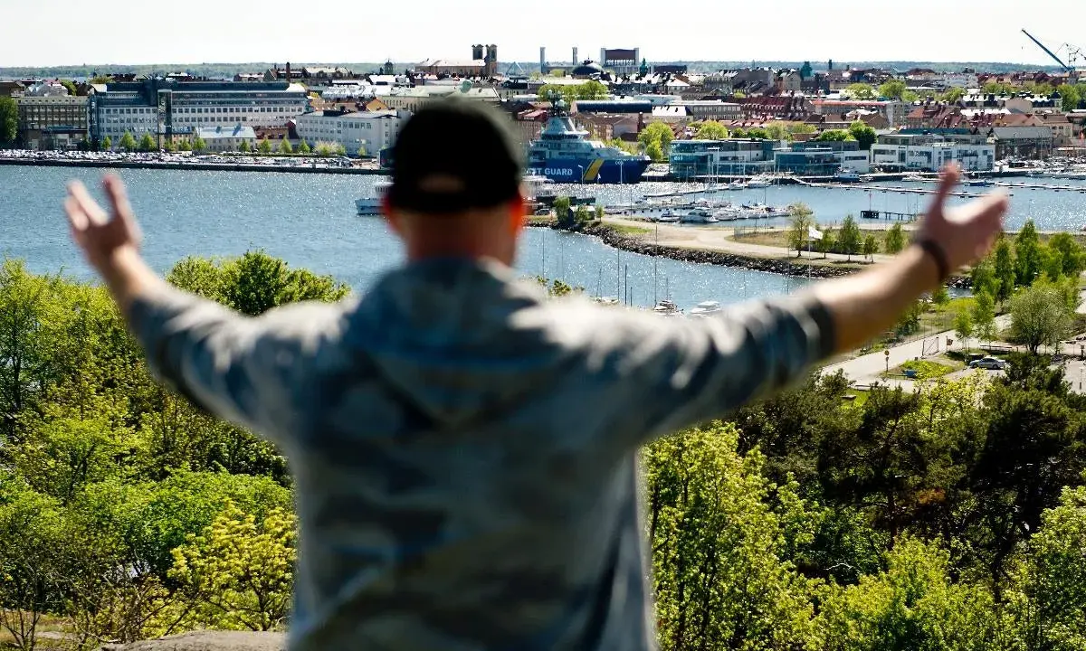En person med armarna utsträckta njuter av utsikten över en hamn och stad, kanske den soligaste staden i Sverige.