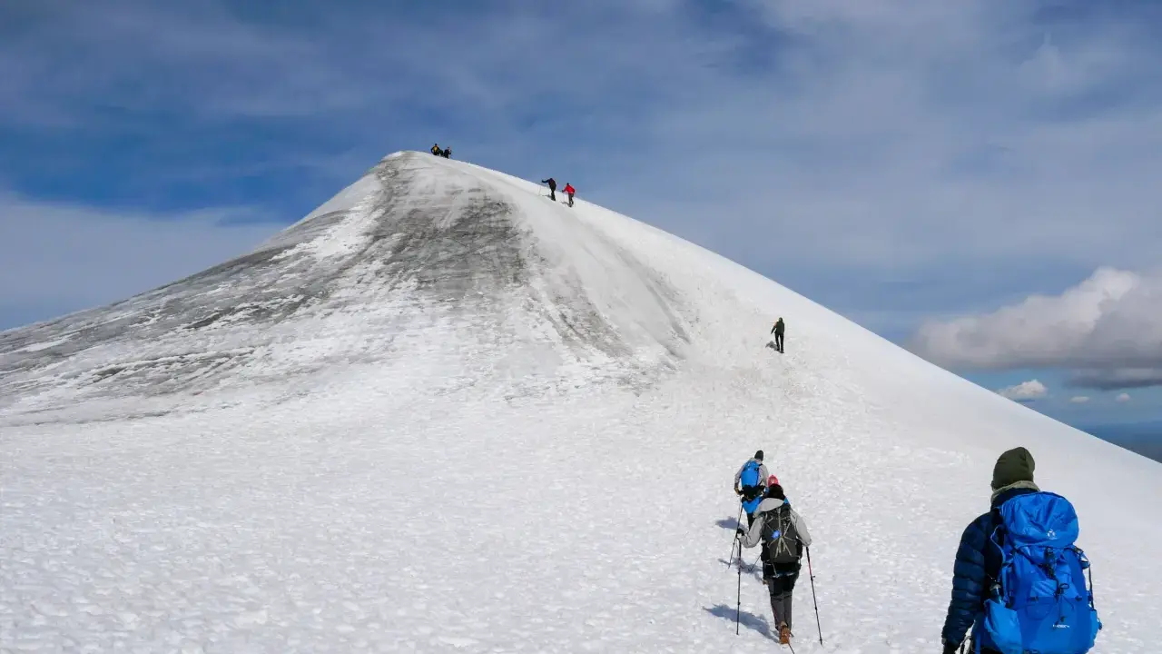 Vandrare klättrar uppför en snöig sluttning mot Kebnekaises topp. En bra packlista för Kebnekaise är avgörande för en säker och njutbar tur.