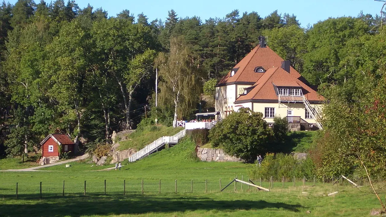 Gula huset vid grinda Stockholm, med röda stugor och grönskande träd.