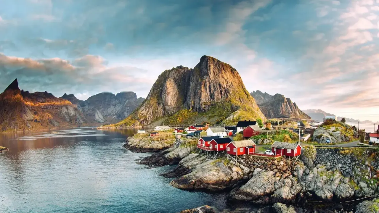 Röda fiskestugor vid en vik, med dramatiska berg i bakgrunden. En idyllisk vy som visar var ligger Lofoten.