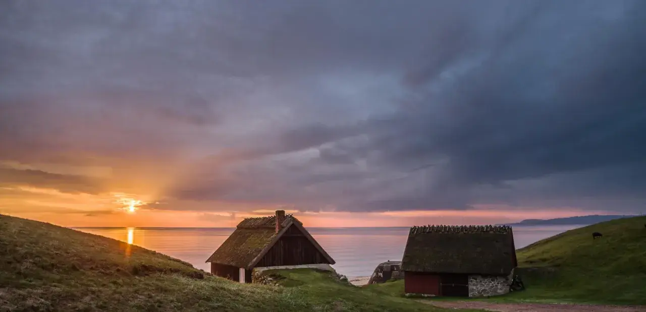 Två gamla hus med halmtak vid havet i Skåne Tranås. Solnedgången färgar himlen orange och lila.