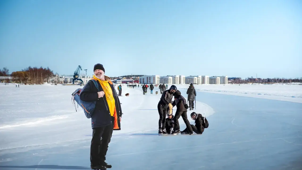 Glad man med ryggsäck njuter av en solig dag på isen i Luleå. Folk åker skridskor och promenerar i bakgrunden.
