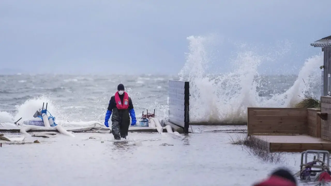 Person i flytväst och stövlar går genom vatten under en storm i Danmark. Vågor slår mot land.