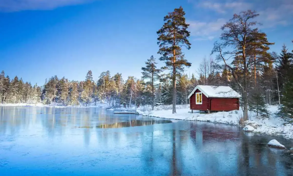 En röd stuga vid en isbelagd sjö i Sverige, perfekt för en mysig julresa.