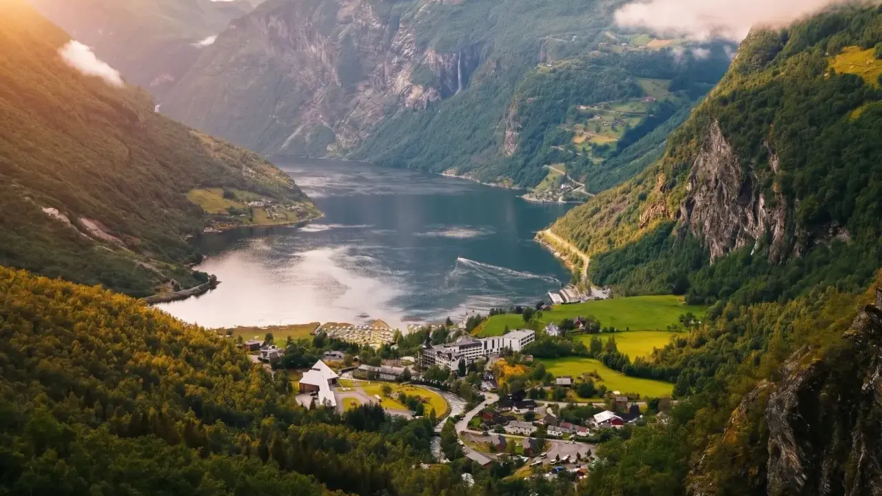 Majestätisk natur i Norge med en djup fjord, branta berg täckta av grönska och ett litet samhälle vid vattnet.