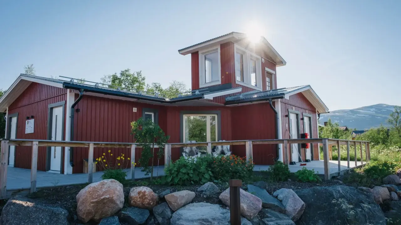 Rött hus med vita knutar och en solig veranda. Abisko Turiststation välkomnar besökare till fjällen.