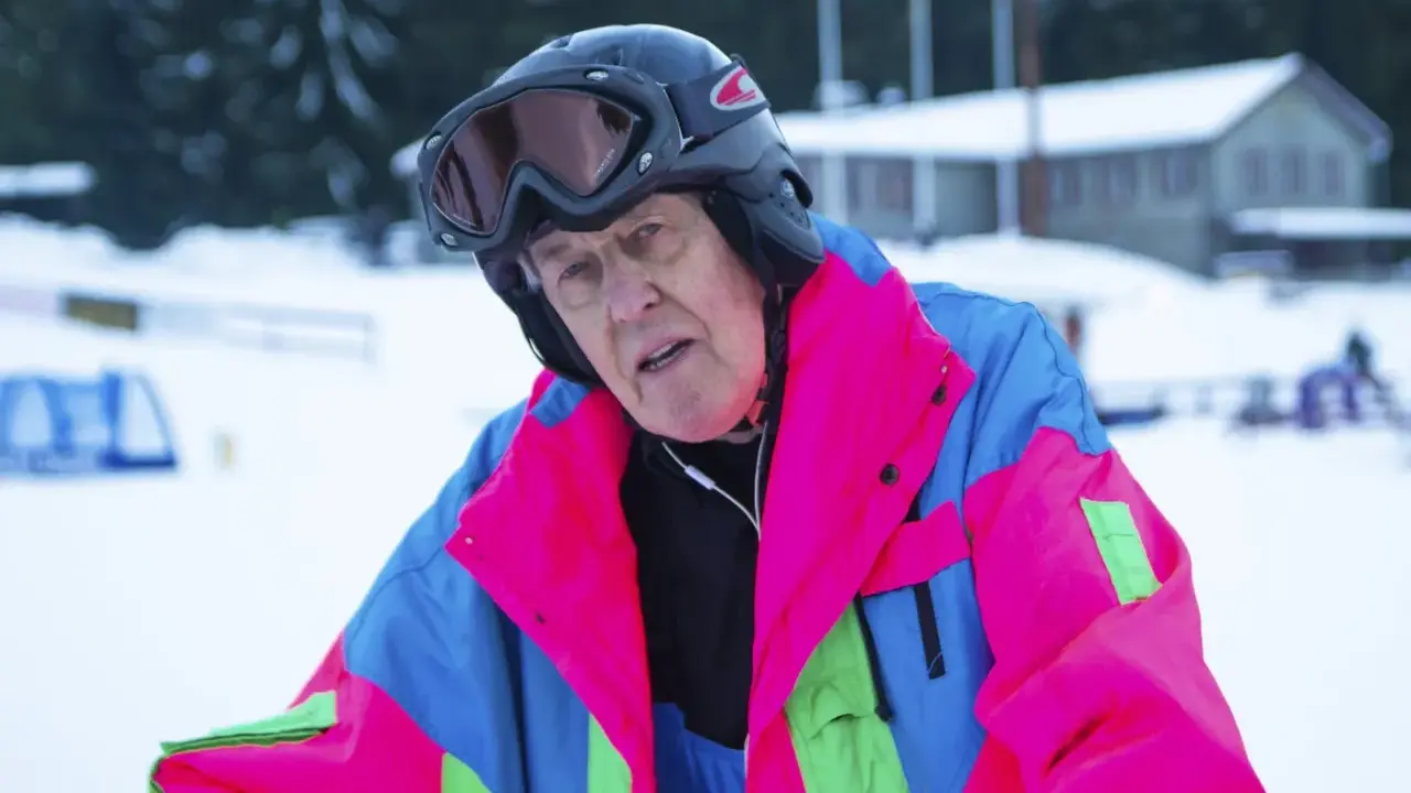 Äldre man i färgglad skidjacka och hjälm, redo för backen. Kanske en veteran från Edsbyn skidor.