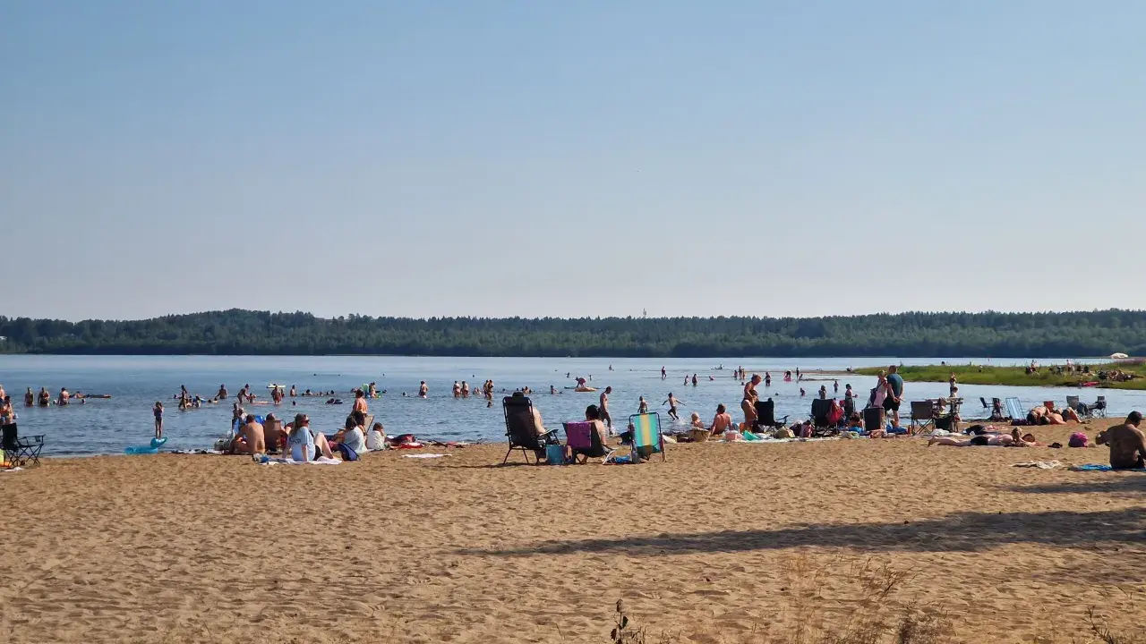 Folk njuter av solen och badar vid en strand, en perfekt plats för camping i Luleå.