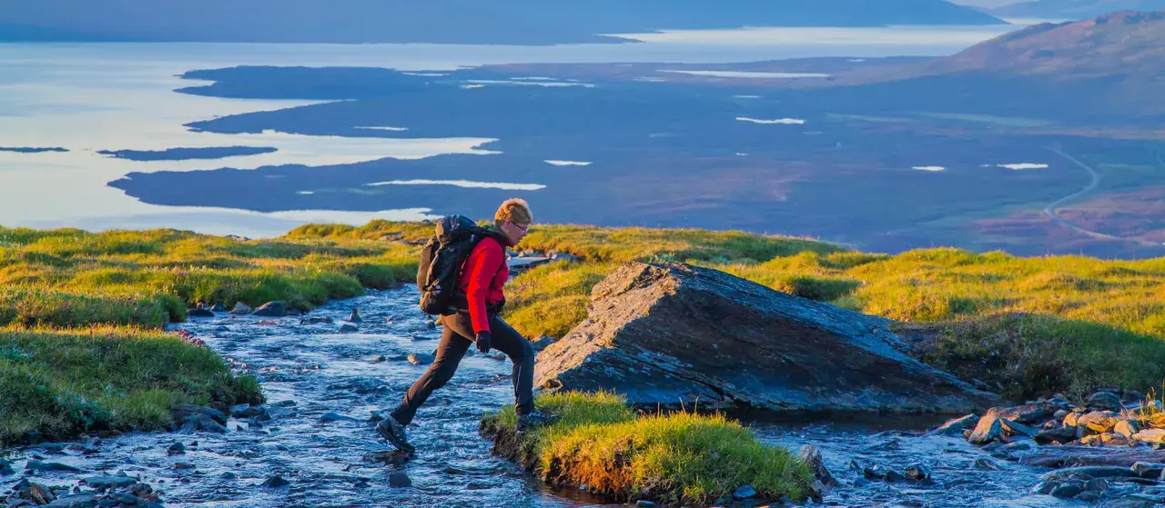 Vandrare korsar en bäck i Abisko, med Kebnekaise-massivet i bakgrunden.