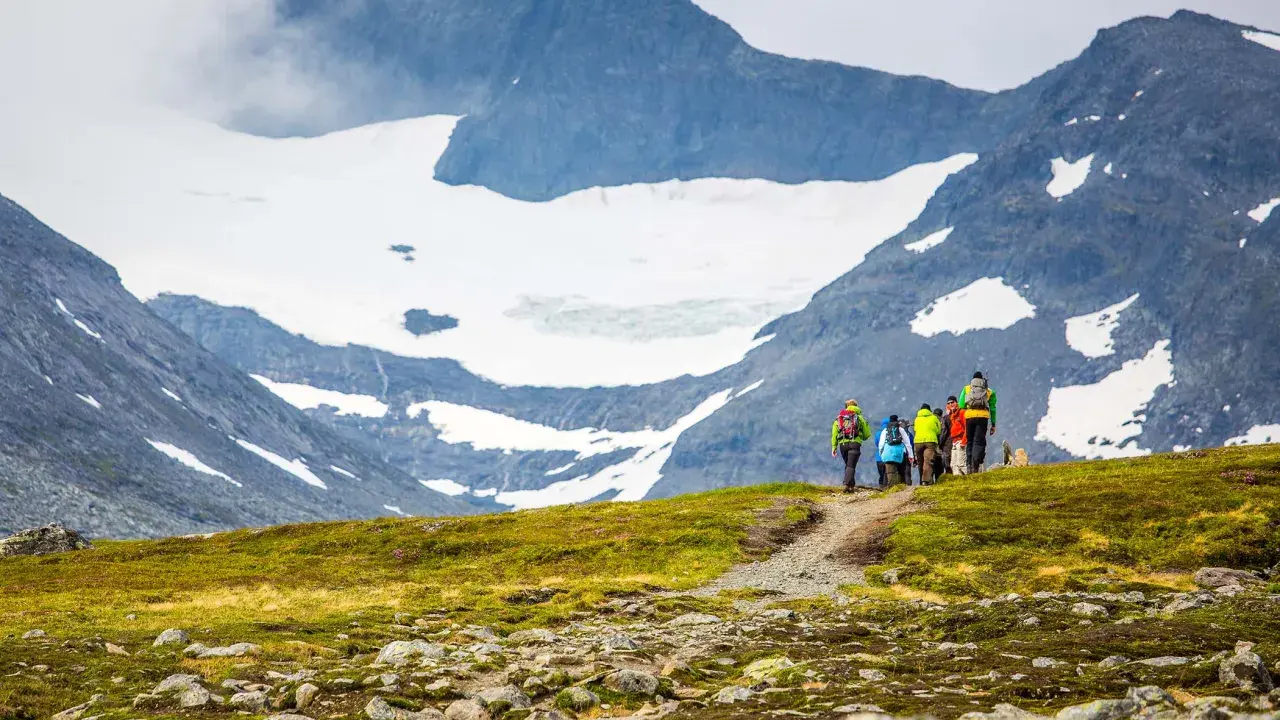 Vandrare med ryggsäckar går längs en stig med glaciärklädda sylarna runt.