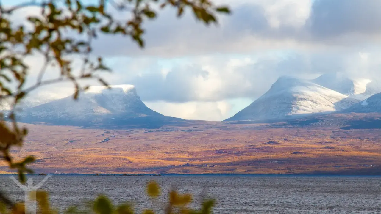 Vacker vy över Lapporten i Abisko, Sverige. Snöklädda berg reser sig över en höstfärgad tundra vid en sjö.
