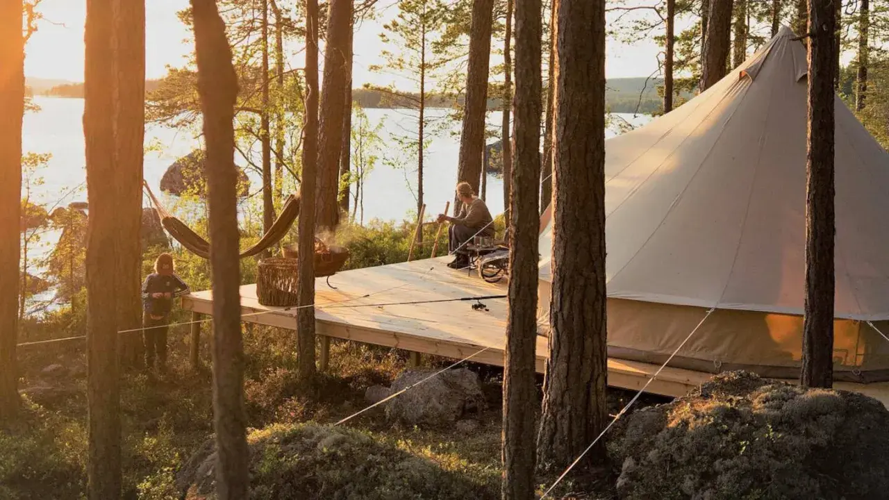 Kloten Nature Resort: en man sitter på en altan vid en sjö, bredvid ett stort tält. En hängmatta och en eldskål syns också.