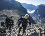 Vandring uppför stenigt landskap mot Sveriges högsta berg. Moln och bergstoppar i bakgrunden.