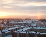 Vintermorgon i Boden, Sverige. Solen går upp över ett snötäckt landskap med hus och träd.