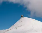 Vandrare på toppen av en snötäckt bergstopp, en vy som ger en känsla av var ligger Kebnekaise.