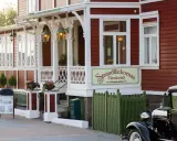 Strandflickornas Havshotell i Lysekil, en charmig röd byggnad med vita detaljer, välkomnar besökare. En klassisk bil står parkerad framför.