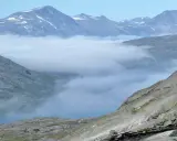 Moln sveper genom dalarna i Padjelanta nationalpark, med snöklädda bergstoppar som reser sig mot en klarblå himmel.