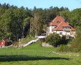 Gula huset vid grinda Stockholm, med röda stugor och grönskande träd.