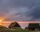 Två gamla hus med halmtak vid havet i Skåne Tranås. Solnedgången färgar himlen orange och lila.