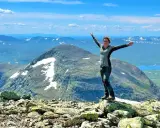 Kvinna med armarna utsträckta på en stenig topp, njuter av utsikten över fjällandskap med snöfläckar. Ett perfekt berg att bestiga!