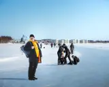 Glad man med ryggsäck njuter av en solig dag på isen i Luleå. Folk åker skridskor och promenerar i bakgrunden.