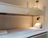 Enkel och mysig våningssäng för ditt arholma boende. Två sängar med vita lakan och varsin läslampa.