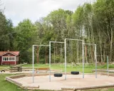 Lekplats med gungor och sandlåda vid en röd stuga, en idyllisk plats som påminner om nyrups naturhotell.