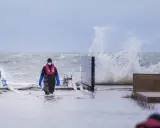 Person i flytväst och stövlar går genom vatten under en storm i Danmark. Vågor slår mot land.