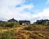 Mörka trähus med solpaneler och en svensk flagga som vajar. Ett charmigt vandrarhem i Dalarna, omgivet av vildmark.