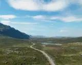Väg slingrar sig genom ett vidsträckt landskap med berg och sjöar. Perfekt för camping i Norrbotten.