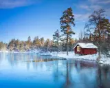 En röd stuga vid en isbelagd sjö i Sverige, perfekt för en mysig julresa.