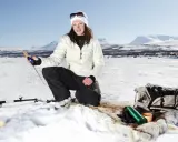 Kvinna ispirar isfiske i Kiruna. Hon har fiskeutrustning och en ryggsäck bredvid sig.