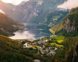 Majestätisk natur i Norge med en djup fjord, branta berg täckta av grönska och ett litet samhälle vid vattnet.