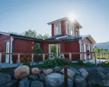 Rött hus med vita knutar och en solig veranda. Abisko Turiststation välkomnar besökare till fjällen.