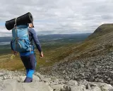 Vandrare med ryggsäck och liggunderlag på väg nerför en stenig fjällsida. En perfekt packlista vandring för äventyret.