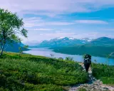 Vandra i Norrland med storslagen utsikt över sjö och snöklädda berg. En ensam vandrare med ryggsäck går på en stenstig.