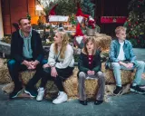 Familj njuter av en mysig stund vid en juldekoration med tomtar och gran. En härlig svensk julkänsla.