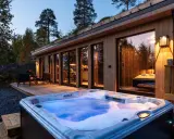 En bubblande badtunna framför en modern stuga i Norge. Trädäck, utemöbler och en grönskande takterrass skapar en mysig atmosfär.