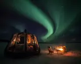 Drömmen att bo i igloo och se norrsken blir verklighet. En glaskupol med säng och en mysig eldstad utomhus under en magisk himmel.