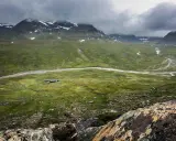 Vacker vy över fjällandskap med snöklädda toppar, en slingrande älv och stugor vid Kungsleden nära Hemavan.