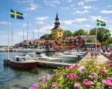 En livlig hamn med svenska flaggor, båtar och röda hus. Kanske en vy från ett mysigt hotell i Norrbotten en solig sommardag.
