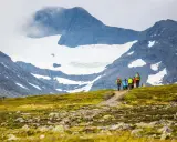 Vandrare på väg mot STF Blåhammaren med snöklädda berg i bakgrunden.