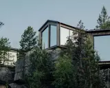 Moderna trähus med stora fönster klättrar uppför en stenig sluttning, omgivna av tallar. En idyllisk camping Lapland resort.