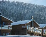 Vinteridyll vid STF Sylarna. Trähus med snötyngda tak och balkonger, mot en tät, snötäckt granskog.