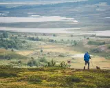 Vandrare med blå ryggsäck på Kungsleden, med vidsträckt landskap av sjöar och kullar.