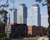 Höga, moderna skyskrapor reser sig bakom tegelbyggnader. En grönskande gren ramar in vyn, som om den undrar när sommaren startar i Sverige.