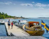 En kvinna och ett barn går på en brygga vid en sjö i Sverige. Båtar ligger förtöjda, en med svensk flagga. En perfekt familjesemester i Sverige.