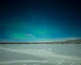 Norrsken dansar över ett fruset hav i Sverige. Snö och stjärnor lyser upp den kalla natten.